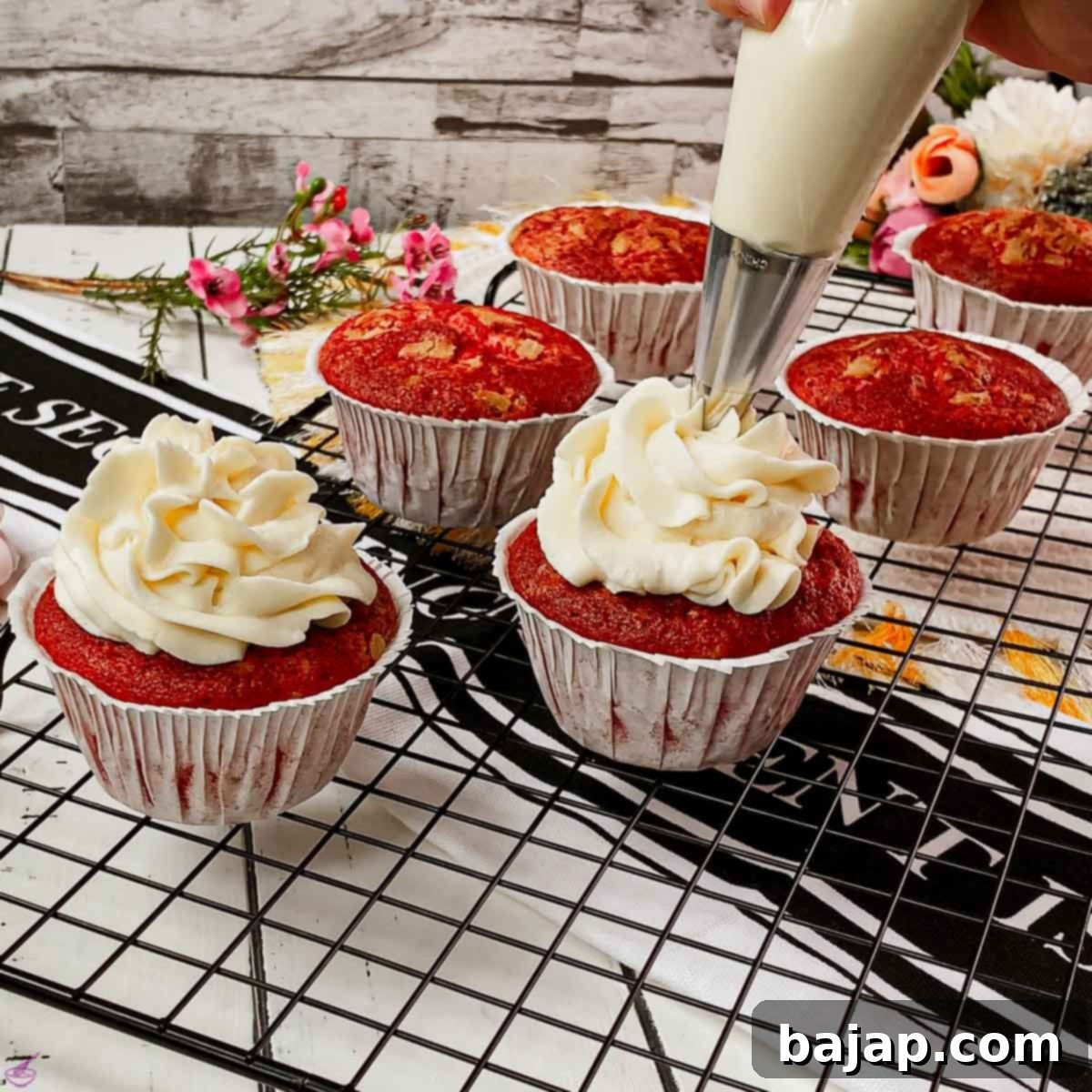 Piping cream cheese frosting on top of red velvet muffin, second layer.