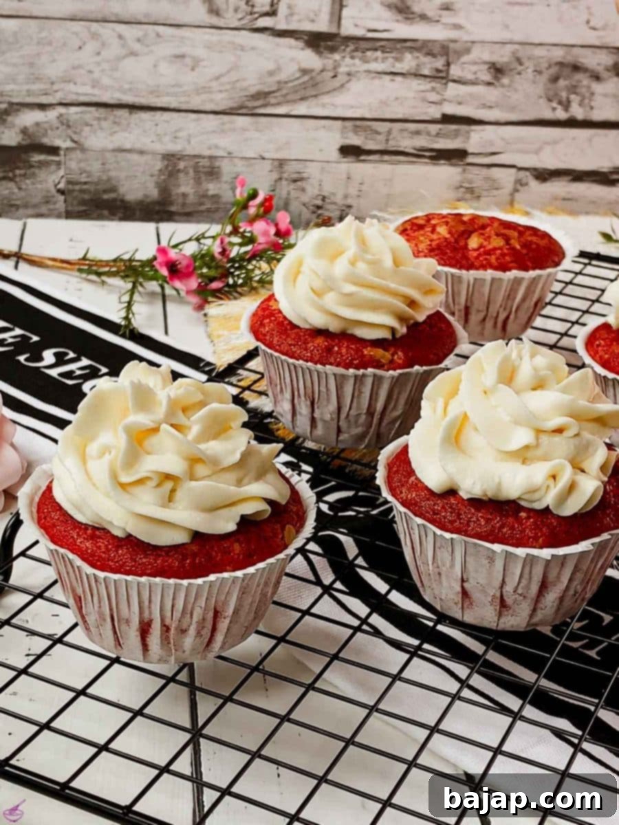 Cream cheese frosting on top of red velvet muffin, set on a cooling rack, styled with a purple background.
