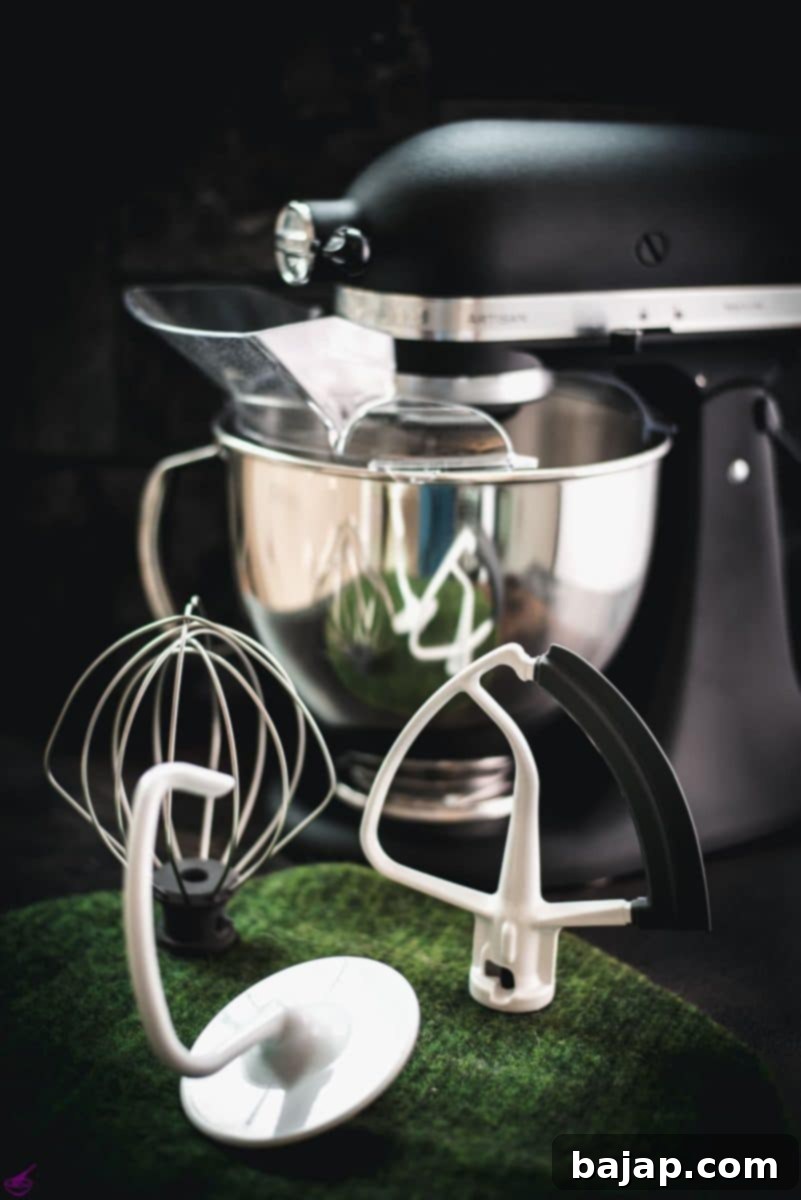 Matt black Kitchenaid stand mixer with various accessories placed on a green felt mat.