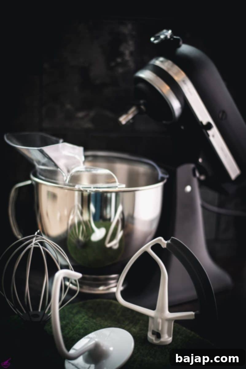Matt black Kitchenaid stand mixer with various accessories placed on a green felt mat.