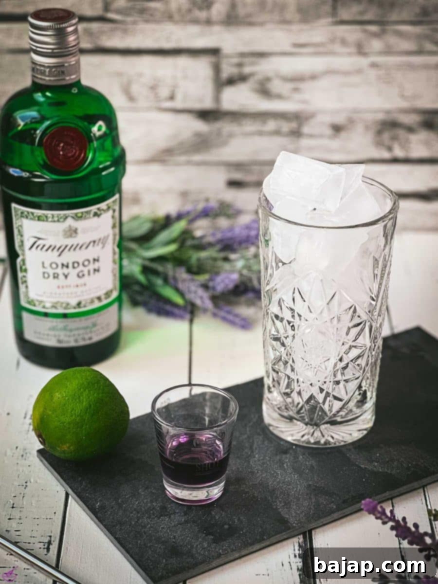 Lavender Gin and Tonic: Your Guide to Botanical Bliss 3 Highball glass filled with cubed ice, next to lavender syrup filled glass and lime. In the back a bottle of Tanqueray London dry gin.