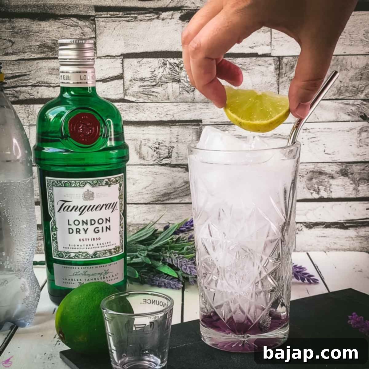 Lavender Gin and Tonic: Your Guide to Botanical Bliss 7 Hand placing a lime wedge on top of a highball glass filled with cubed ice, lavender syrup, gin and tonic.
