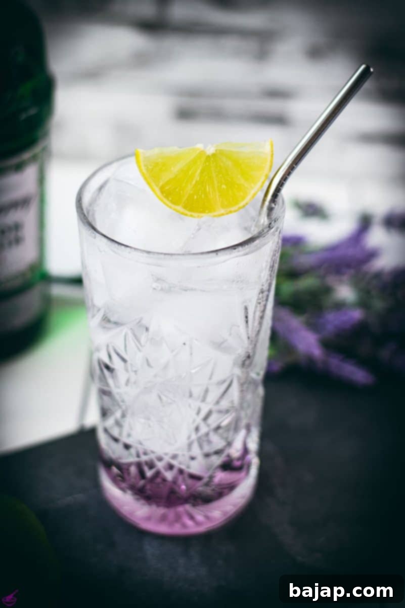 Lavender Gin and Tonic: Your Guide to Botanical Bliss 8 Highball glass filled with lavender gin and tonic, garnished with lime wedge and straw. Placed on black slate plate.