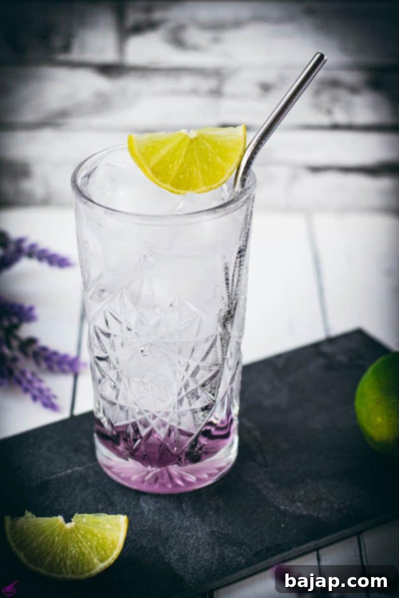 Lavender Gin and Tonic: Your Guide to Botanical Bliss 9 Highball glass filled with lavender gin and tonic, garnished with lime wedge and straw. Placed on black slate plate.
