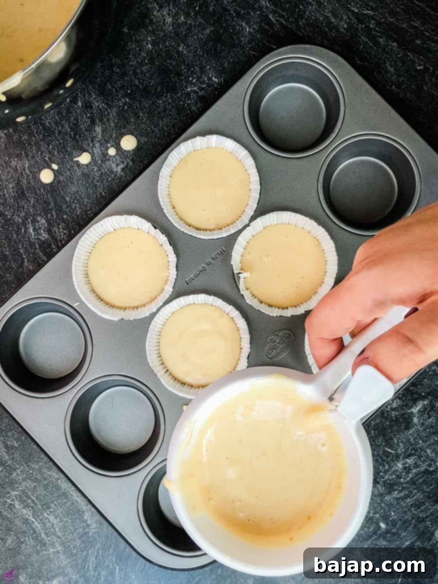 Pouring the fluffy lavender lemon muffin batter carefully into prepared muffin liners using a precise batter dispenser tool, ensuring even distribution for perfectly baked treats.