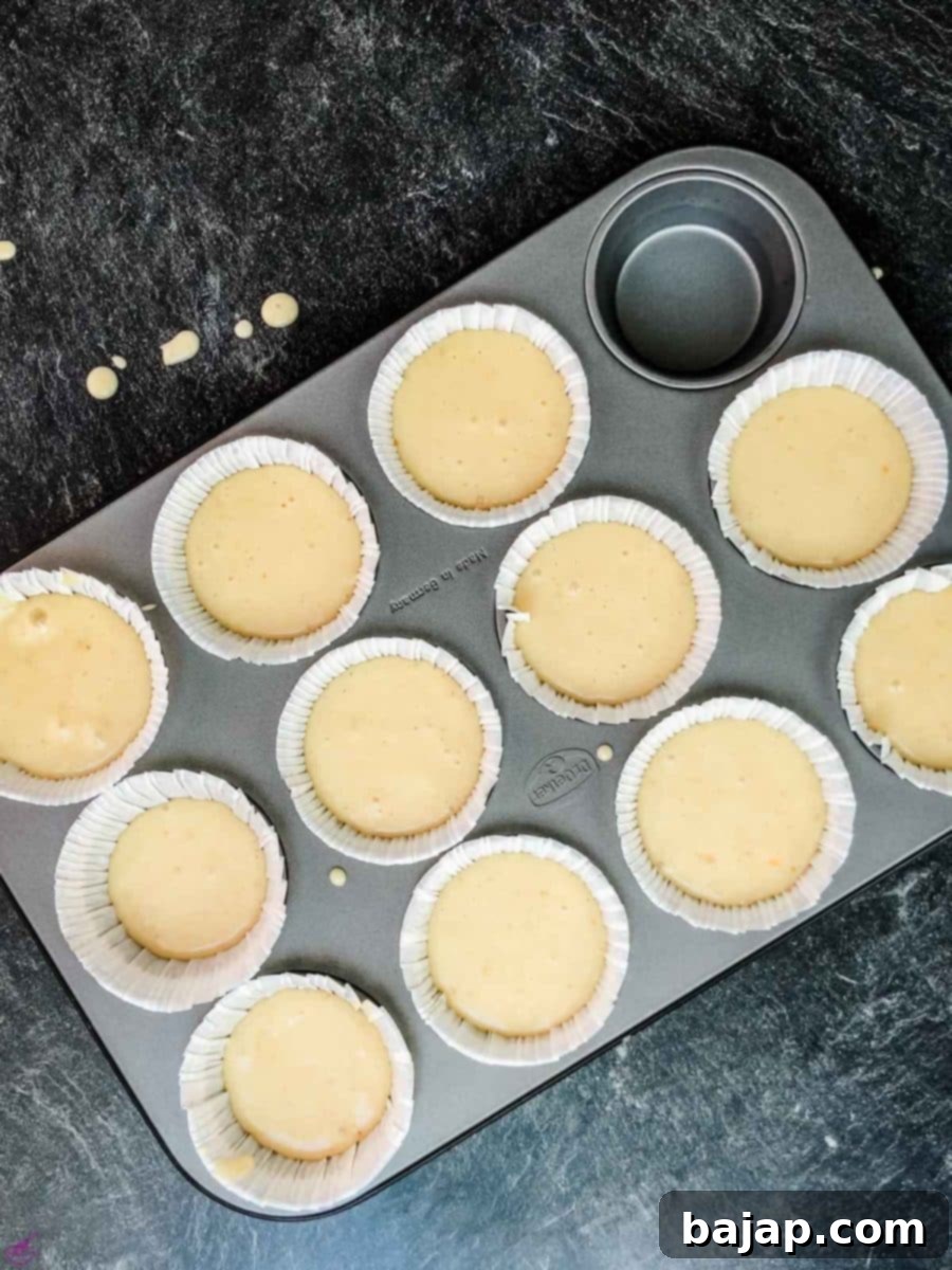 Muffin batter neatly filling individual muffin liners in a baking tray, perfectly prepped and ready for the oven. Each cup contains the promising blend of lavender and lemon, poised to transform into delightful muffins.