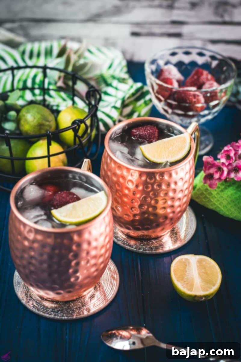 Gorgeous copper cups filled with delicious strawberry Moscow mule placed on blue wooden ground.