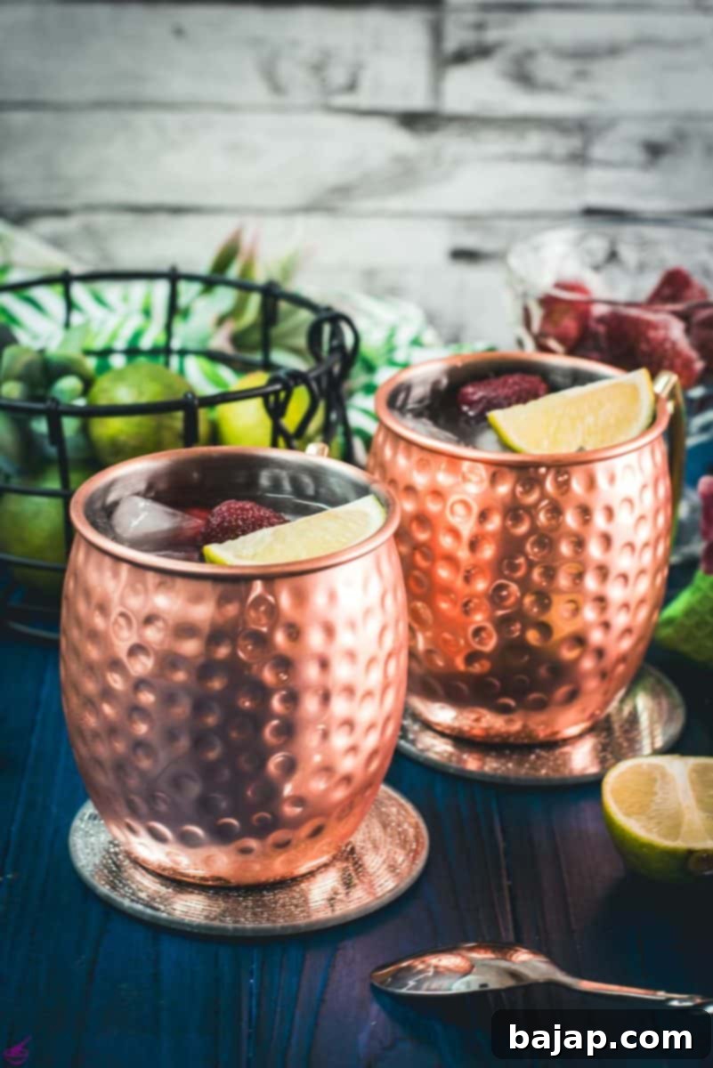 Gorgeous copper cups filled with delicious strawberry Moscow mule placed on blue wooden ground.