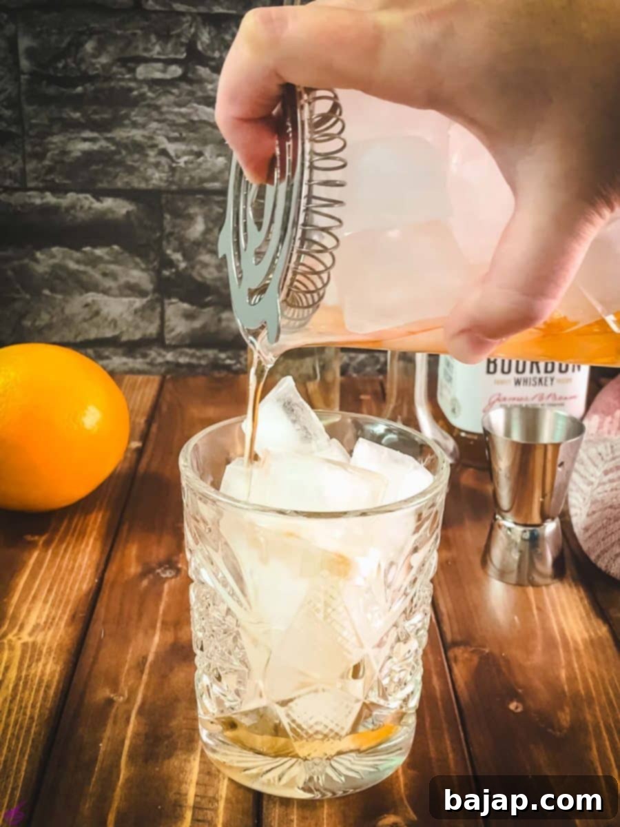 The Old Fashioned cocktail being slowly poured from the stirring glass into the rocks glass.