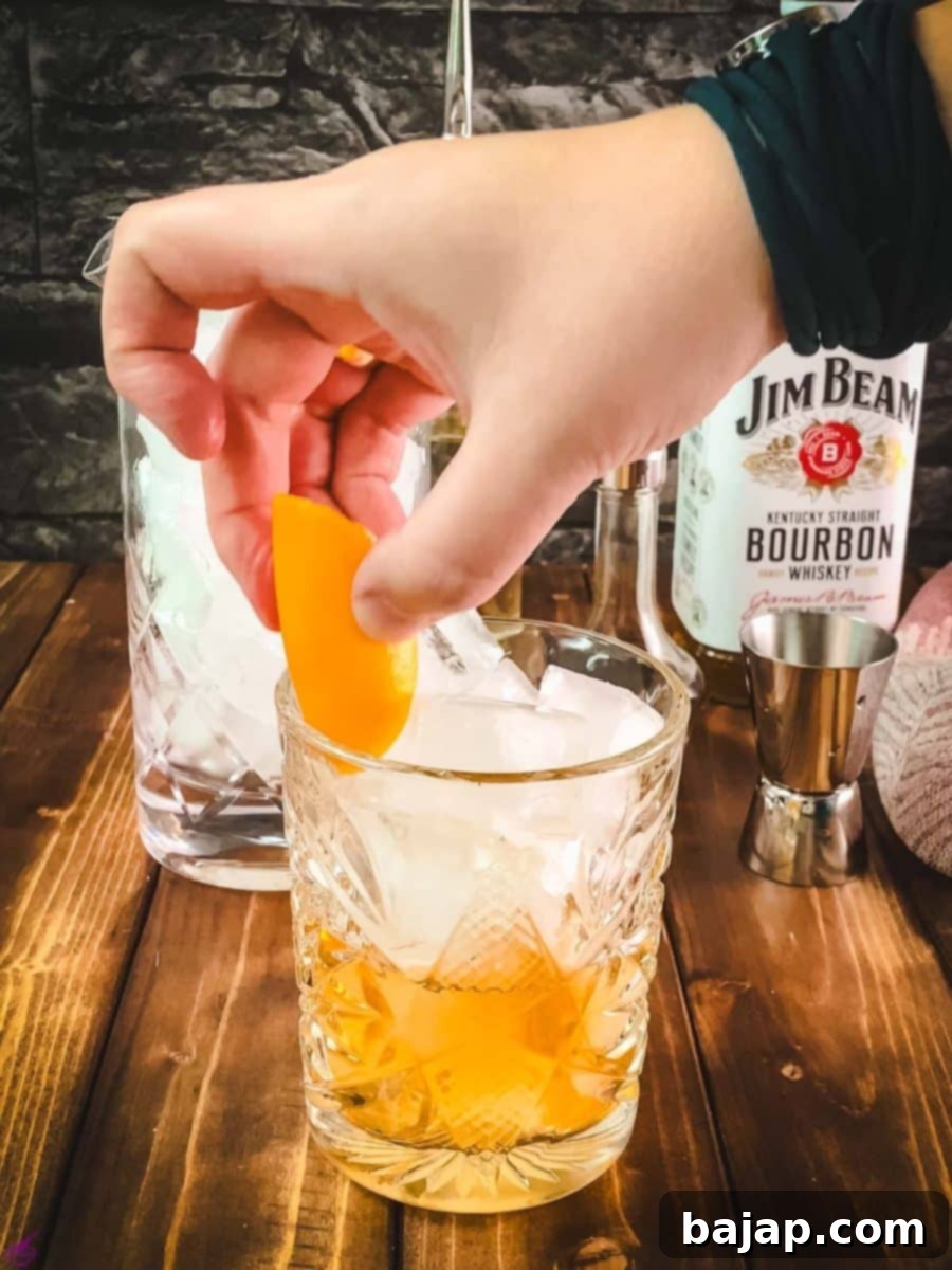 Adding a fresh orange disc as a garnish to the finished Old Fashioned cocktail.