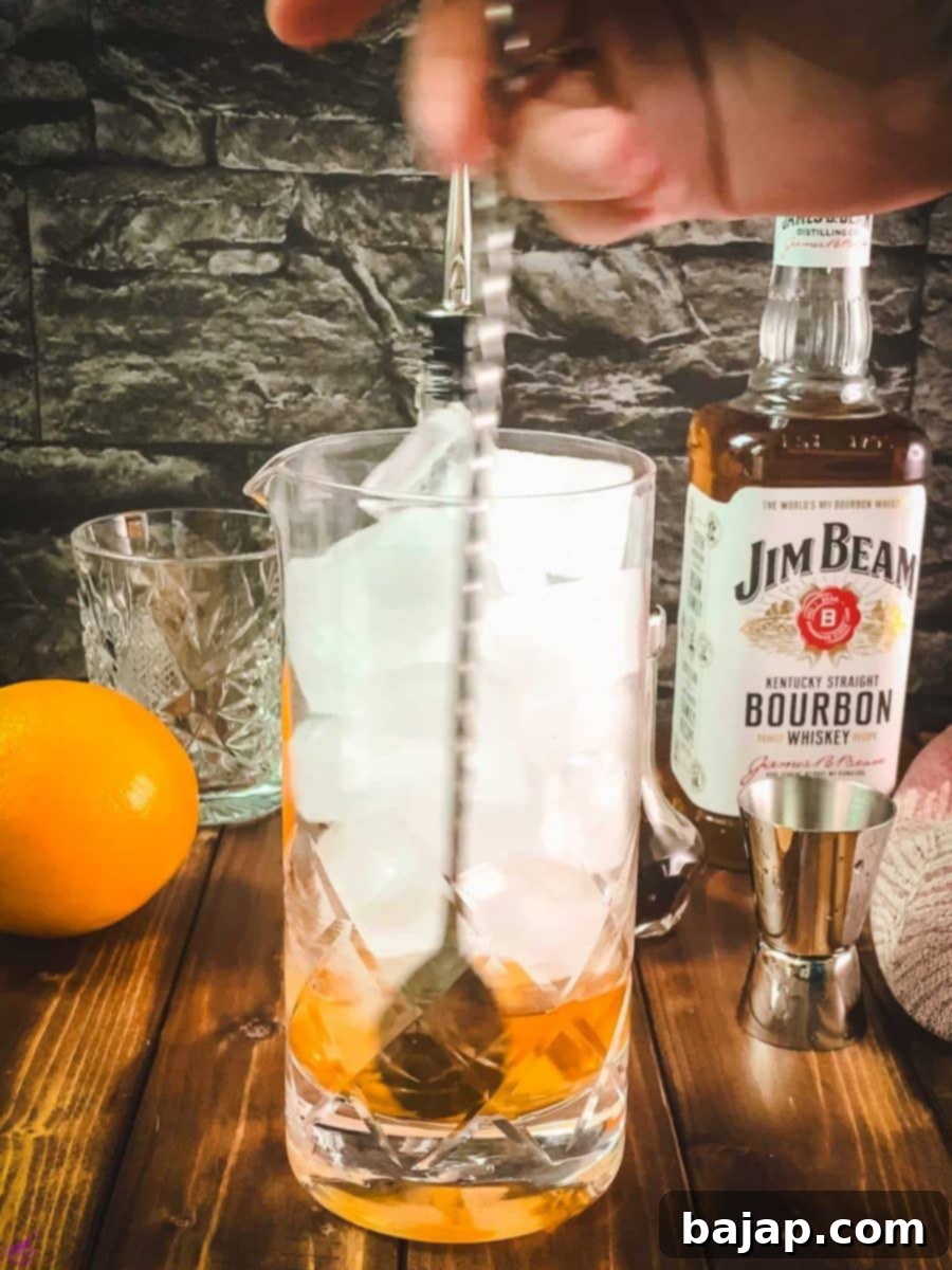 A bar spoon stirring the Old Fashioned cocktail in the glass with ice.