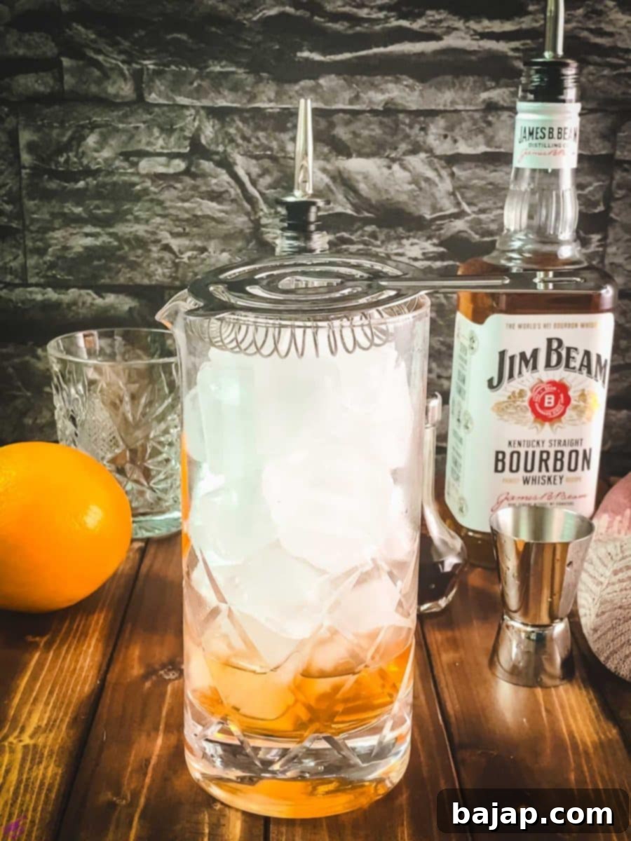 A Julep strainer being used to pour the Old Fashioned into a serving glass, holding back ice.