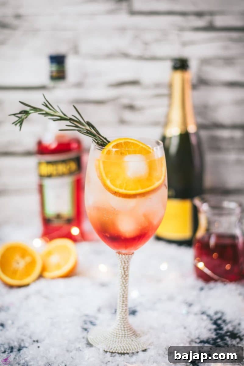 Gorgeous wine glass filled with Winter Aperol spritz, placed on snowy ground.