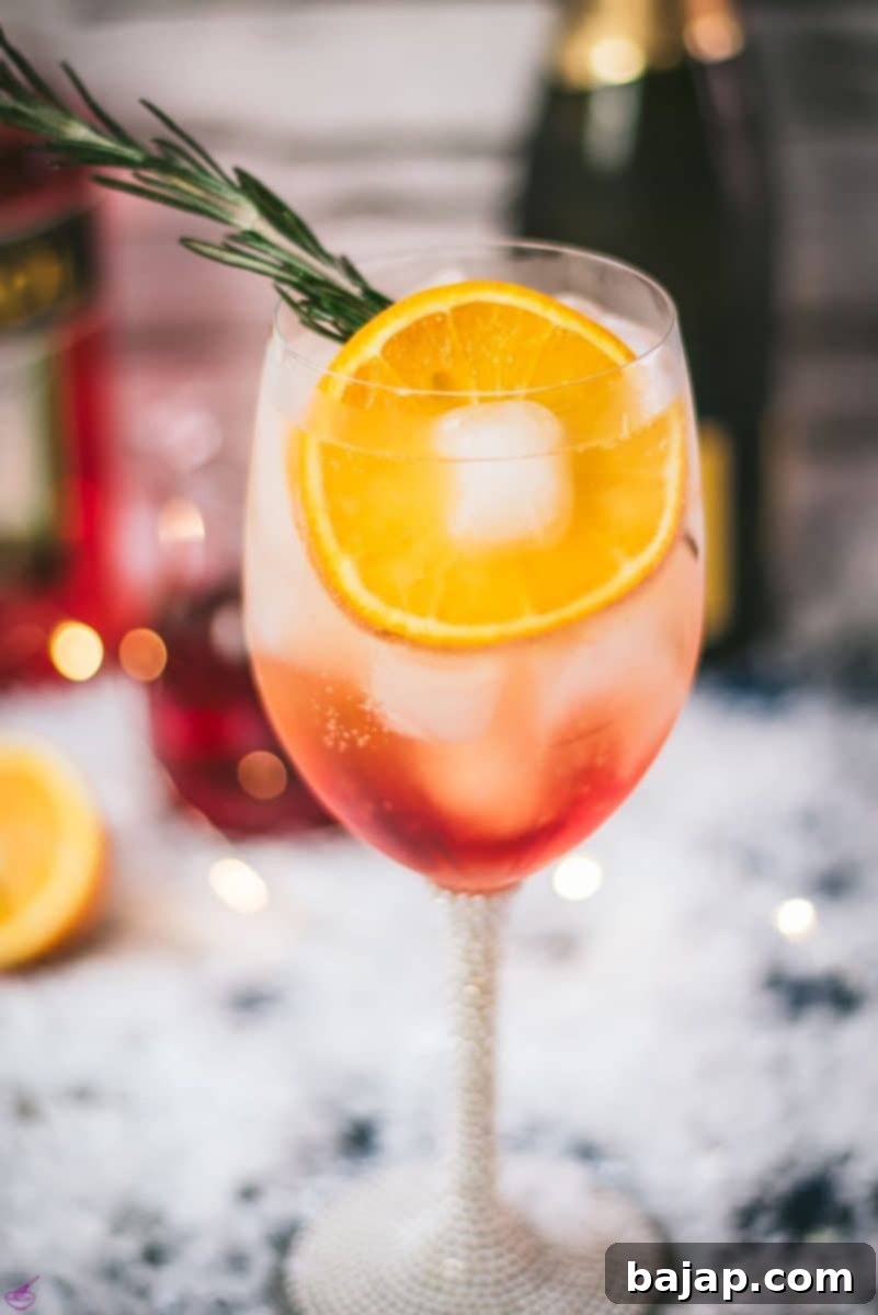 Gorgeous wine glass filled with Winter Aperol spritz, placed on snowy ground.