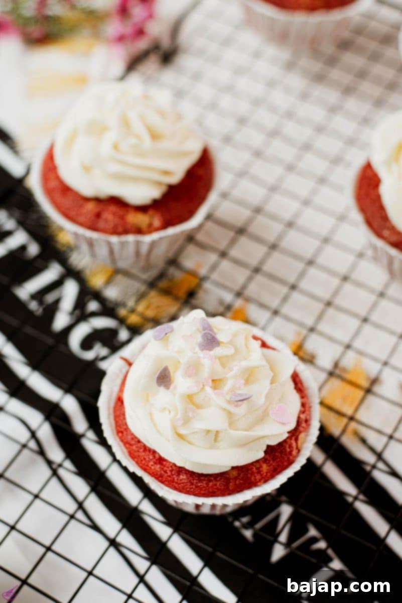 Cream cheese frosting with heart shaped sprinkles on top of red velvet muffin.