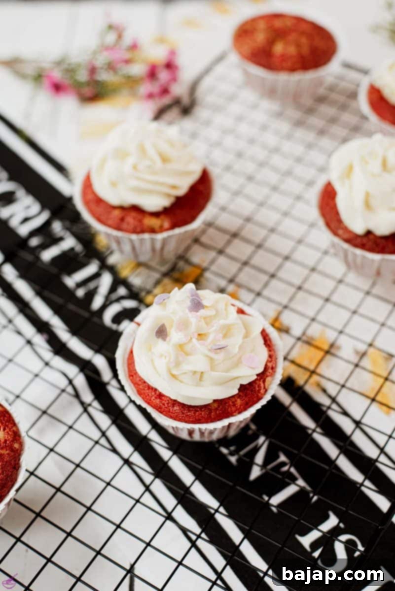 Cream cheese frosting with heart shaped sprinkles on top of red velvet muffin.
