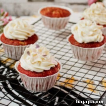 Cream cheese frosting with heart shaped sprinkles on top of red velvet muffin.