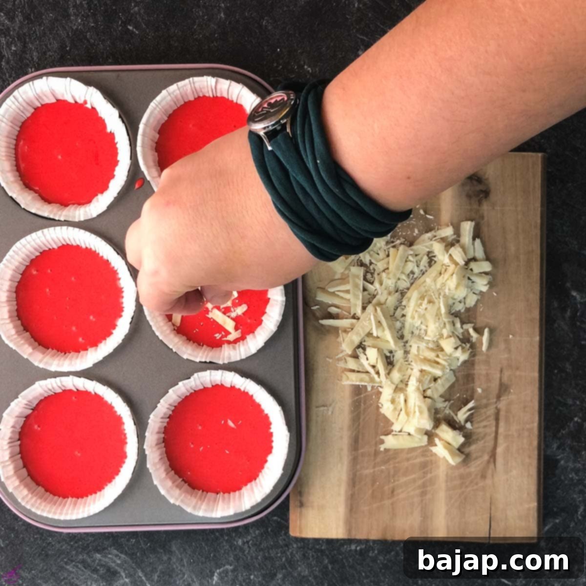Hand sprinkling chopped white chocolate on red velvet muffin dough.
