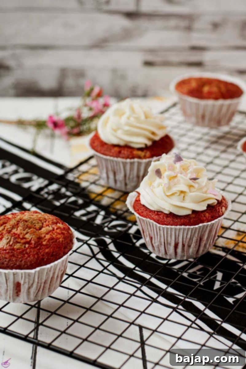 A beautifully piped cream cheese frosting on a red velvet muffin, adorned with delicate heart-shaped sprinkles, showcasing exquisite decoration.