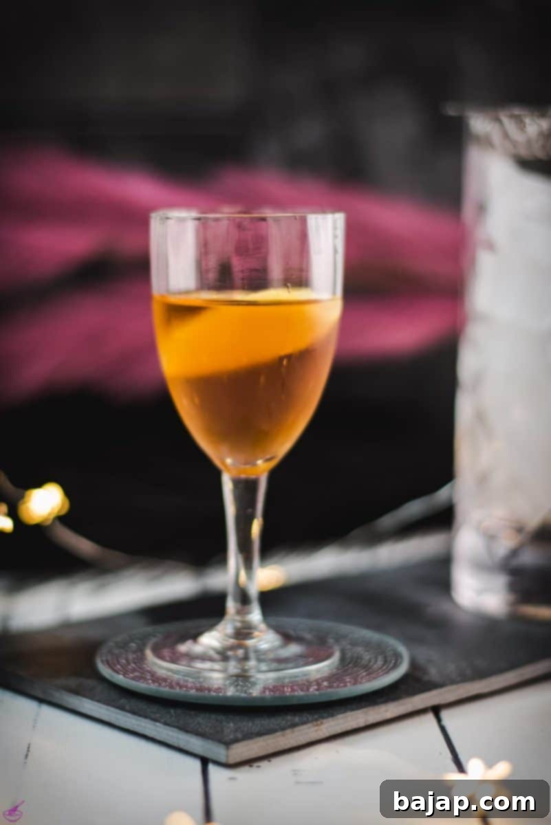 A stunning Martinez cocktail in a Nick & Nora glass, garnished with a vibrant lemon zest, perfectly placed on a sleek black slate surface.