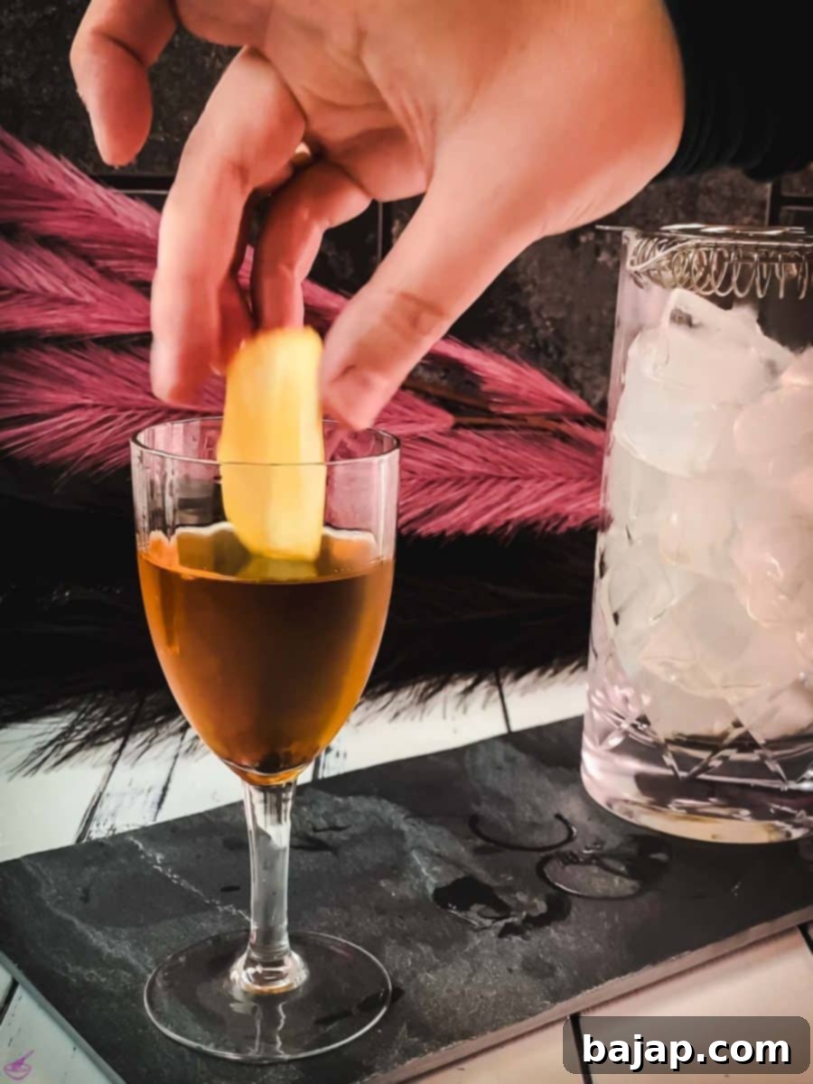 Adding a fresh lemon zest as a garnish to the finished Martinez cocktail, releasing aromatic oils to enhance the drink's citrus profile.