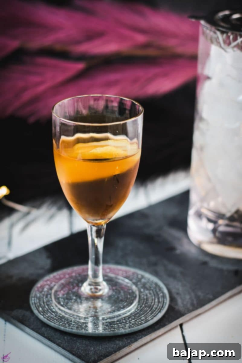 A beautifully presented Martinez cocktail, adorned with a delicate lemon zest, resting elegantly on a dark slate background.