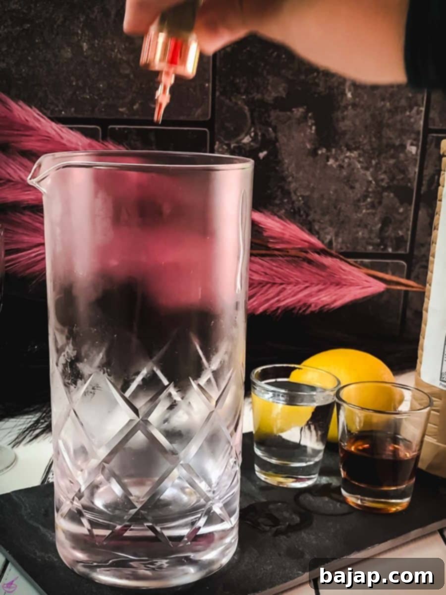 Adding two dashes of fragrant orange bitters to a chilled stirring glass, the first step in crafting a Martinez cocktail.