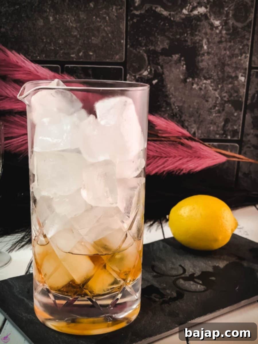 Filling the stirring glass with fresh, cubed ice to begin the chilling and dilution process for the Martinez cocktail.