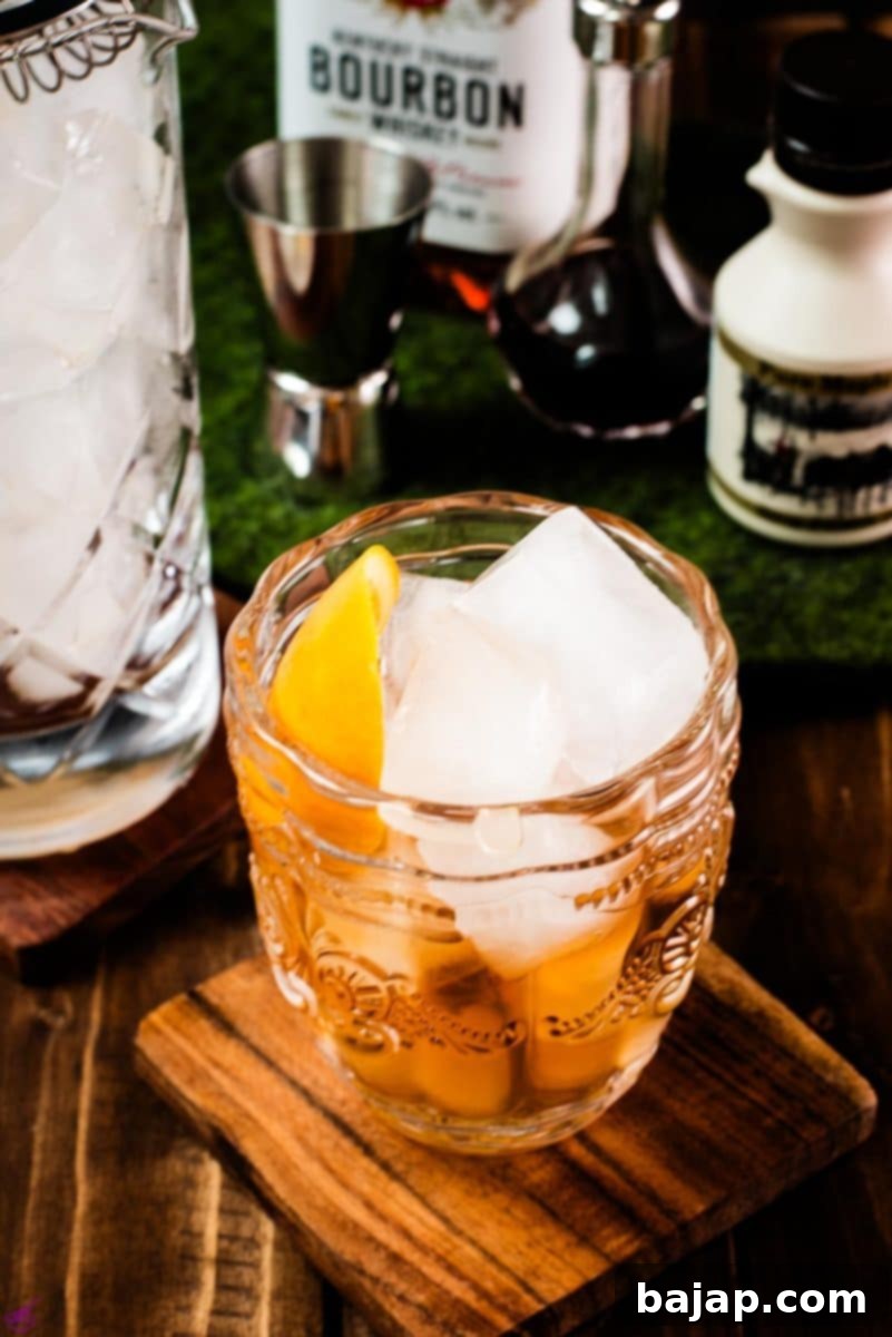 Golden Maple Old Fashioned 2 Gorgeous glass filled with maple old fashioned on wooden coaster. The drink is garnished with an orange zest and placed next to a stirring glass and a maple syrup bottle.