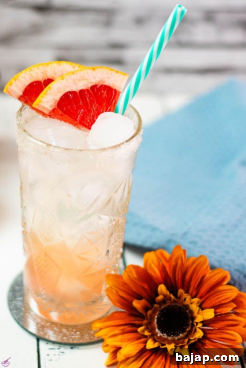 A vibrant and perfectly garnished Paloma cocktail in a highball glass, adorned with grapefruit slices and a straw, ready to be enjoyed.