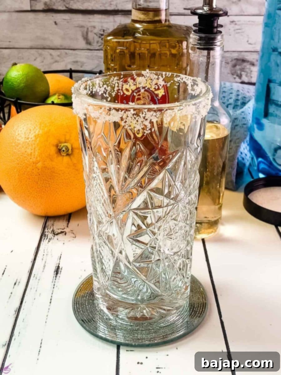 A highball glass with a perfectly finished coarse salt rim, ready for the Paloma ingredients.