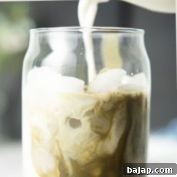 Pouring oat milk into glass with matcha.