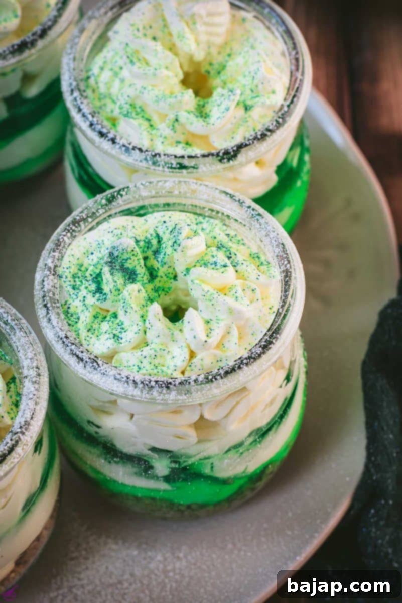 Gorgeous no bake lime cheesecakes in a jar for celebrating St. Patrick's Day! Placed on a white plate sitting on a brown wooden floor.