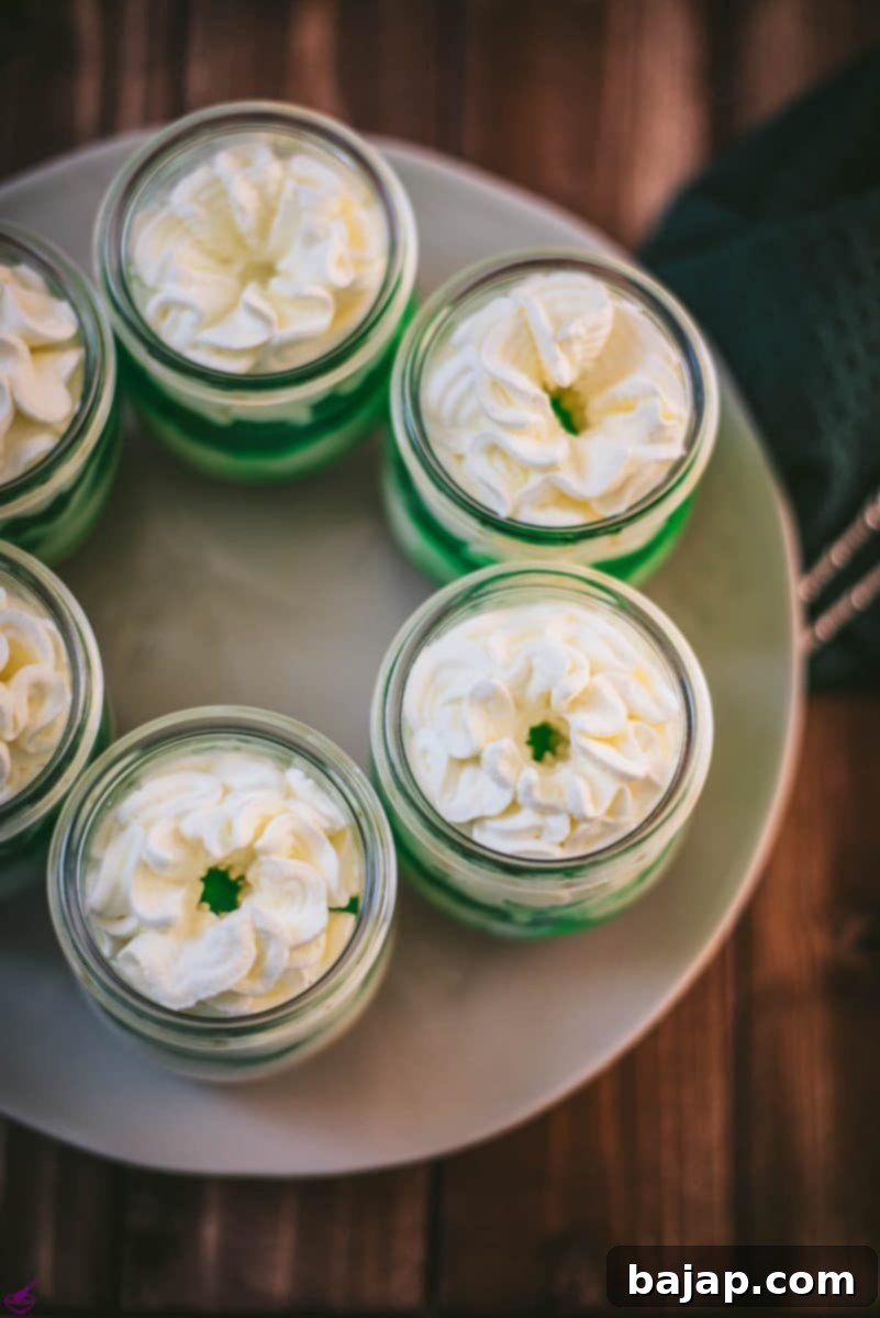 Gorgeous no bake lime cheesecakes in a jar for celebrating St. Patrick's Day! Placed on a white plate sitting on a brown wooden floor.