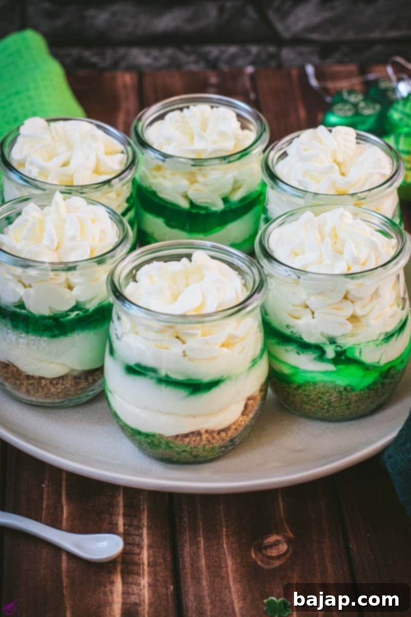 Gorgeous no bake lime cheesecakes in a jar for celebrating St. Patrick's Day! Placed on a white plate sitting on a brown wooden floor.