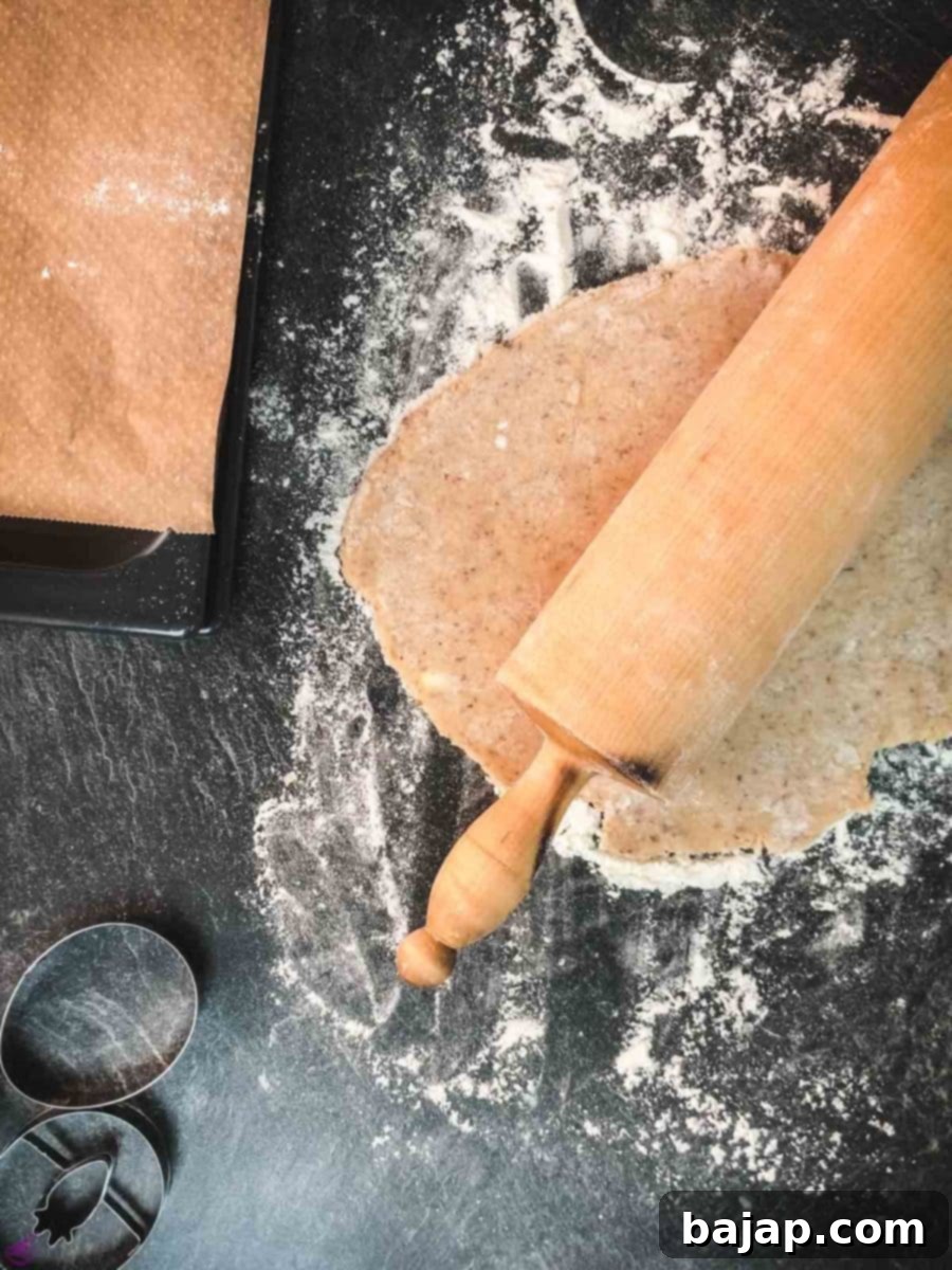 The ground almond cookie dough is being expertly rolled out using a wooden rolling pin on a floured surface, preparing for festive cut-outs.