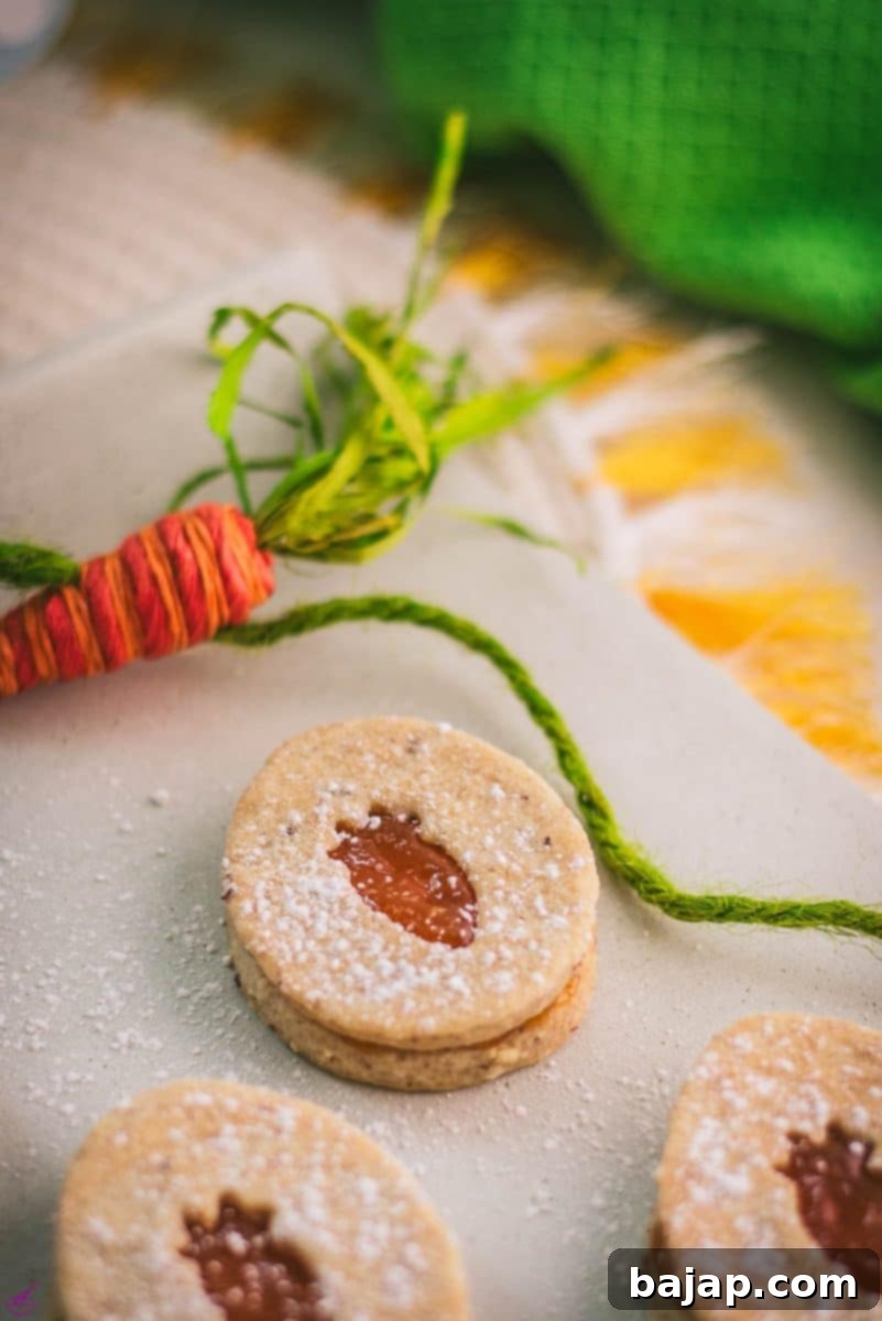 Gorgeous vegan Easter cut out cookies with vibrant apricot jam filling, delicately dusted with powdered sugar, presented on a pristine white stone plate.