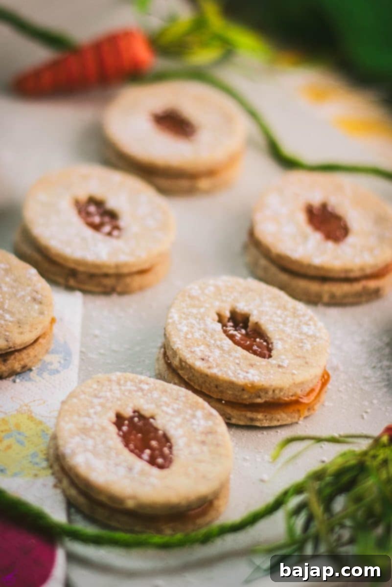 Close-up of beautiful vegan Easter cut-out cookies filled with apricot jam, arranged on a white stone plate, ready to be enjoyed.