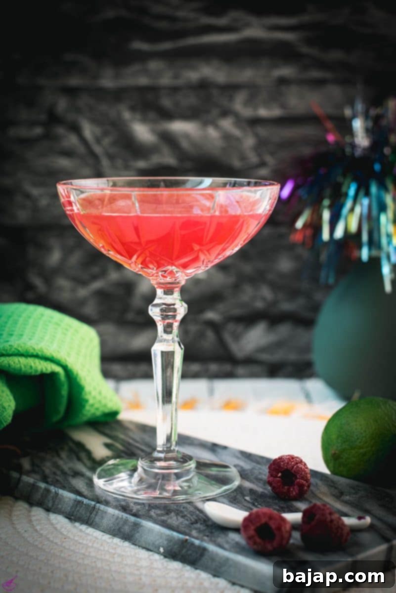 Gorgeous raspberry daiquiri with a vibrant red color placed on marble plate next to three raspberries. The refreshing taste of this drink makes it perfect for hot summer days!