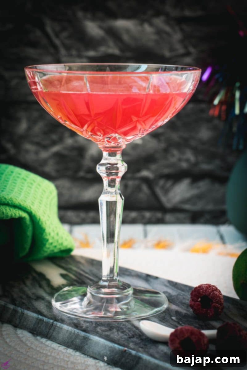 Gorgeous raspberry daiquiri with a vibrant red color placed on marble plate next to three raspberries, showcasing the perfect presentation.