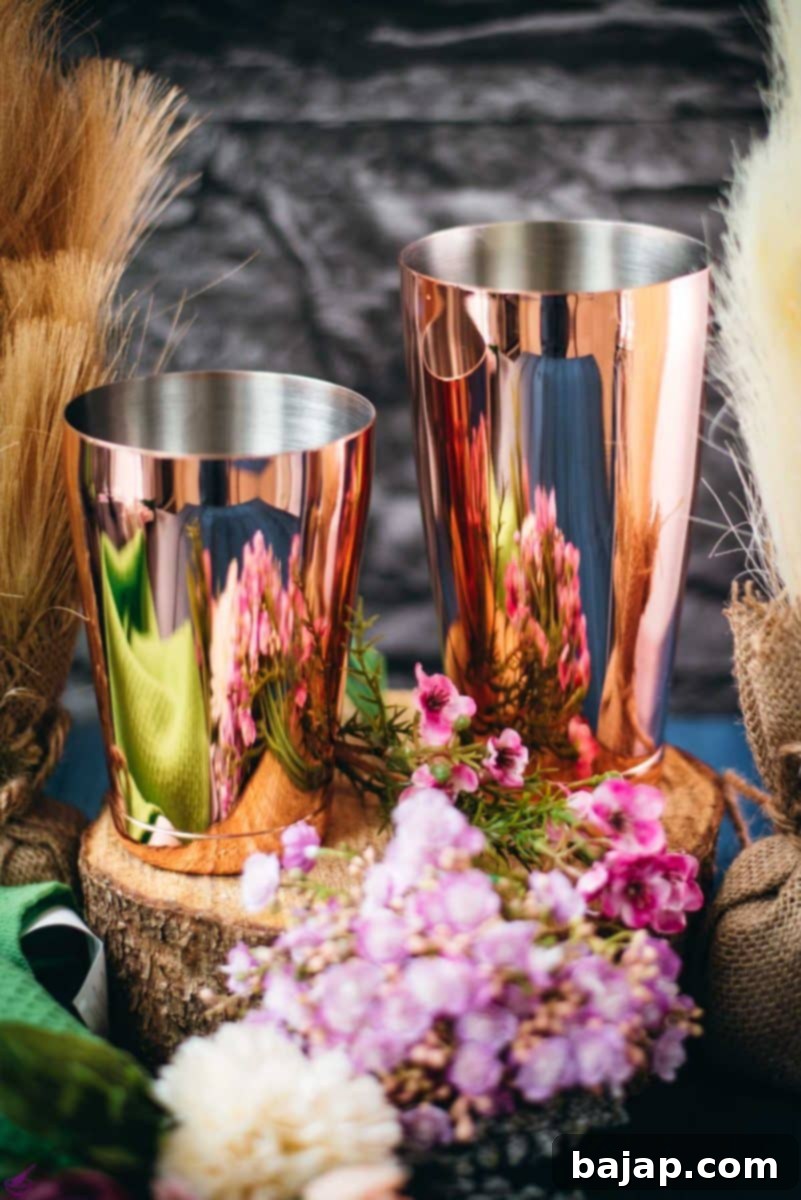Stylish rosé Boston shaker, composed of two nested tins, displayed on a wooden surface beside blooming flowers, symbolizing professional mixology.