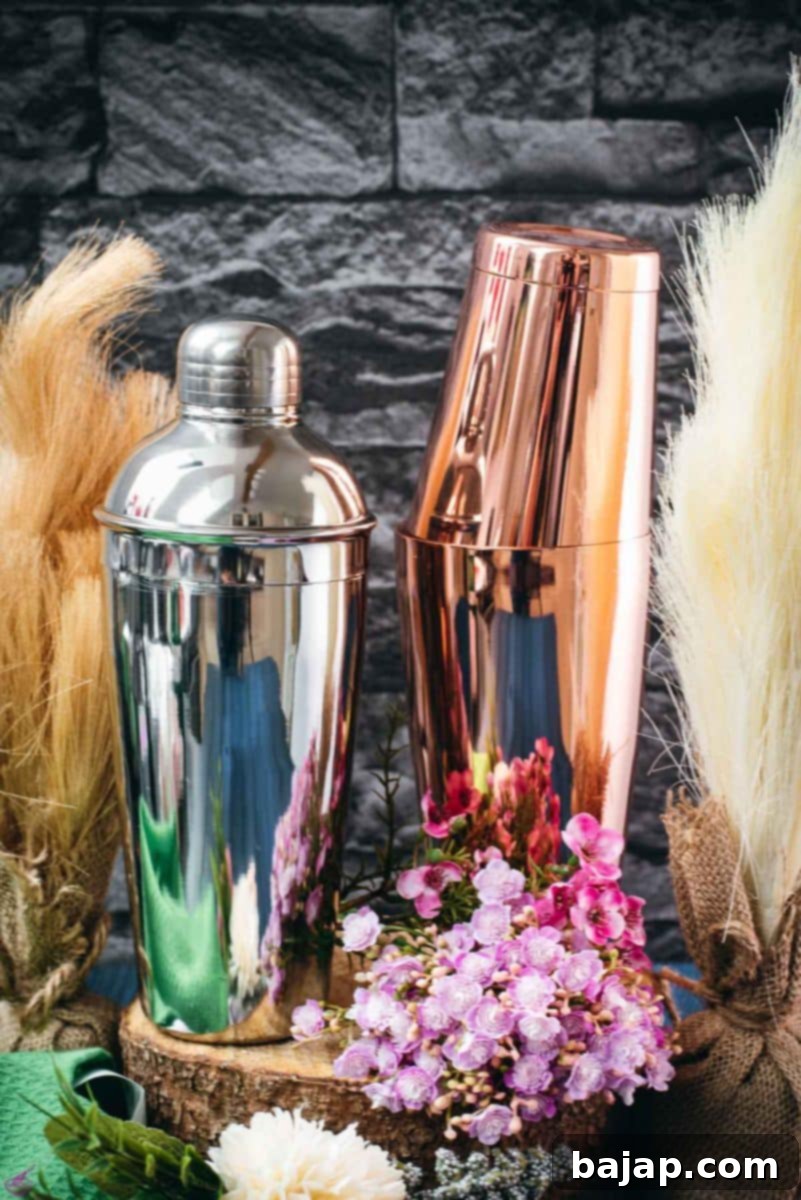 A Cobbler shaker and a Boston shaker stand side-by-side on a wooden surface, nestled among flowers, showcasing the variety of cocktail tools.