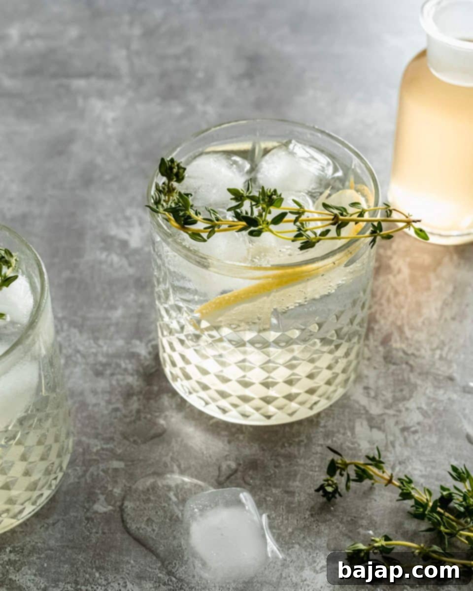 An elegant Elderflower Gin Cocktail with a lemon slice and fresh herbs as garnish.