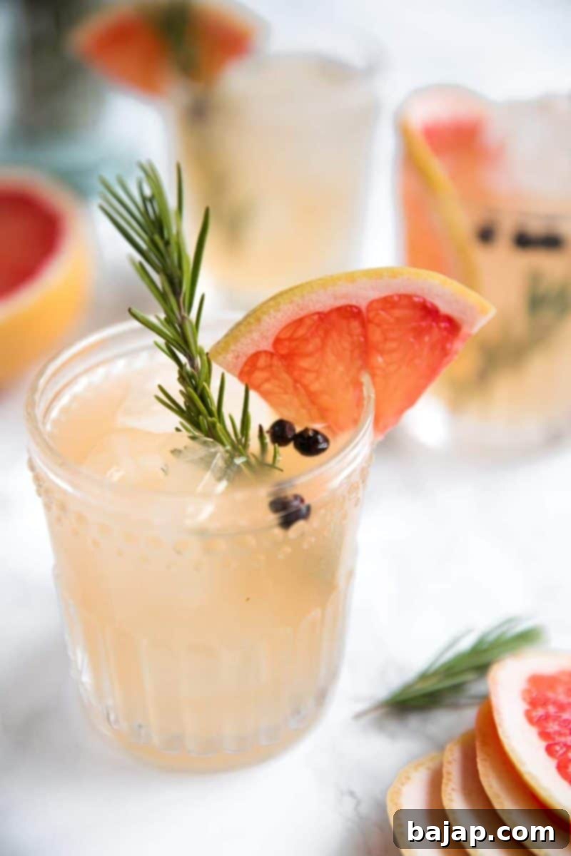 An elegant Elderflower Grapefruit Gin and Tonic garnished with a grapefruit slice and fresh herbs.