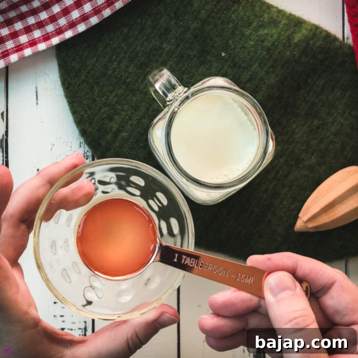 Adding exactly one tablespoon of strained lemon juice to a measuring cup filled with milk, initiating the curdling process.