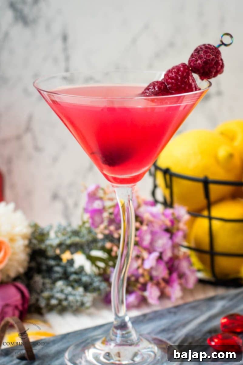 A beautifully presented cocktail glass filled with a delicious raspberry lemon drop martini, garnished with fresh raspberries on a decorative cocktail spike, ready for a special occasion.