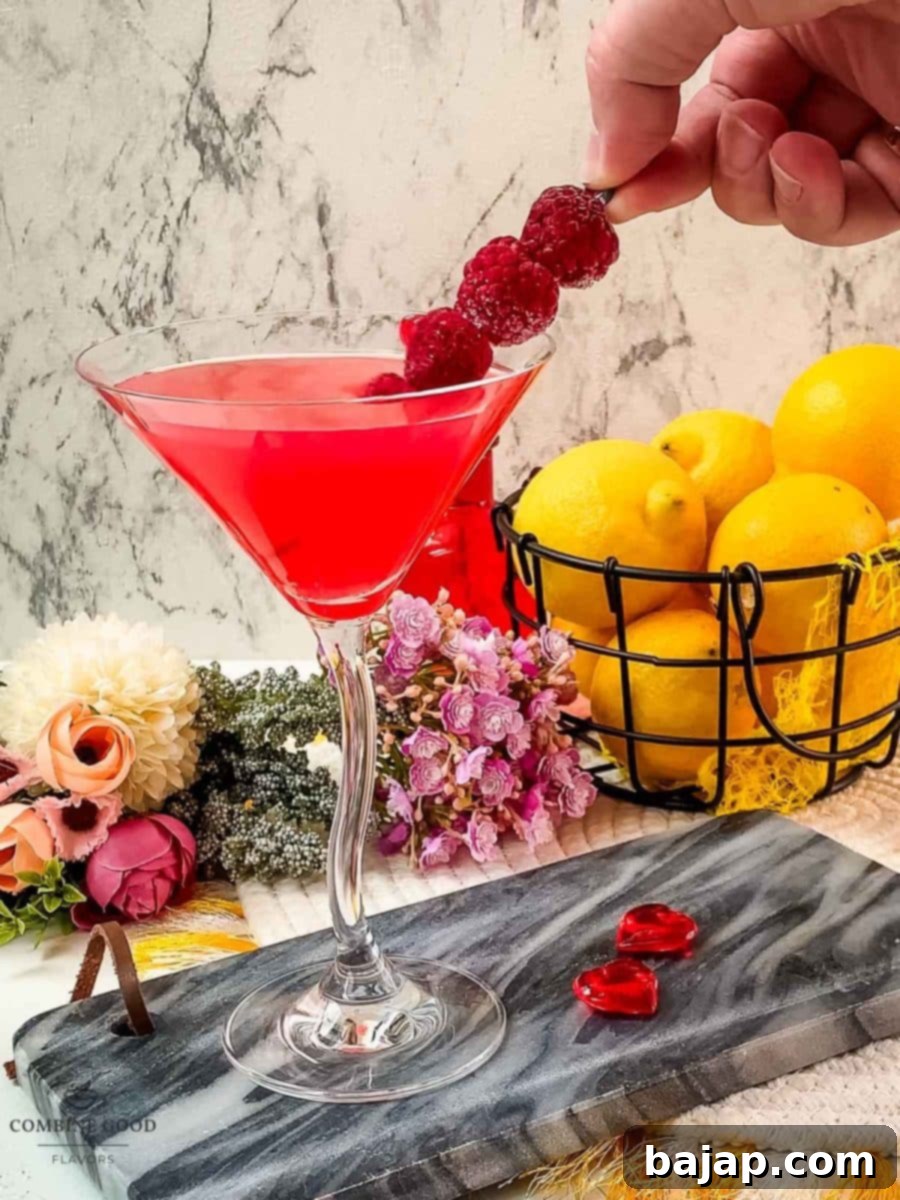 A hand carefully placing a cocktail spike adorned with fresh raspberries into a raspberry lemon drop martini, completing the elegant garnish.