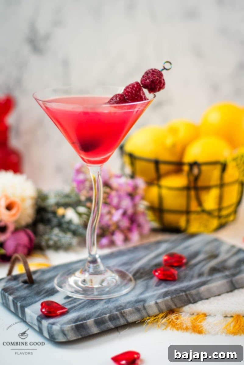 A raspberry lemon drop martini, garnished with fresh raspberries on a cocktail spike, glistening in a perfectly chilled cocktail glass.