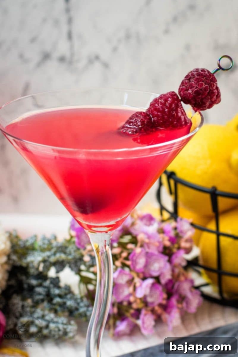A vibrant raspberry lemon drop martini in a frosted glass, beautifully garnished with three fresh raspberries on a cocktail pick, waiting to be enjoyed.