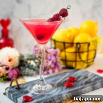 Cocktail glass filled with delicious raspberry lemon drop martini and garnished with raspberries on a cocktail spike.